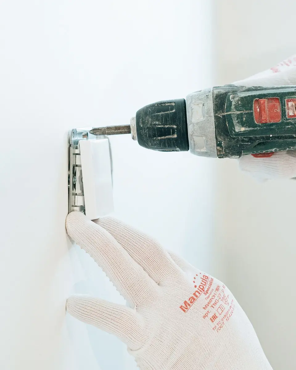 Gloved hands drilling a fixing into a smooth white wall